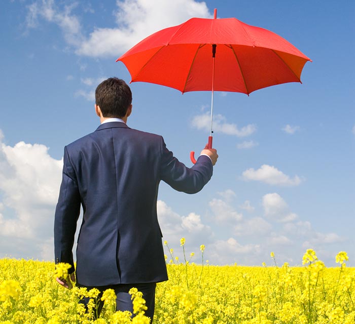 Businessman holding red umbrella over his head in a field.
